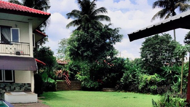 A swimming pool with a stone border, a grassy lawn, and a two-story building with a red roof. - Villa Yosky (Bogor)