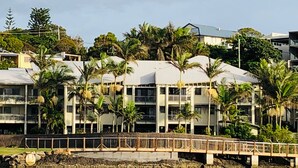 A beachfront hotel with multiple balconies, palm trees, and a wooden bridge over water. - Kingscliff Waterfront - large pool, direct creek access & 5 mins walk to beach (Kingscliff)