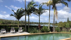 A swimming pool with two lounge chairs and palm trees in the background. - Kingscliff Waterfront - large pool, direct creek access & 5 mins walk to beach (Kingscliff)