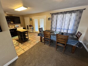 A dining area with a table set for four, a kitchen in the background, and a door leading to a balcony.
