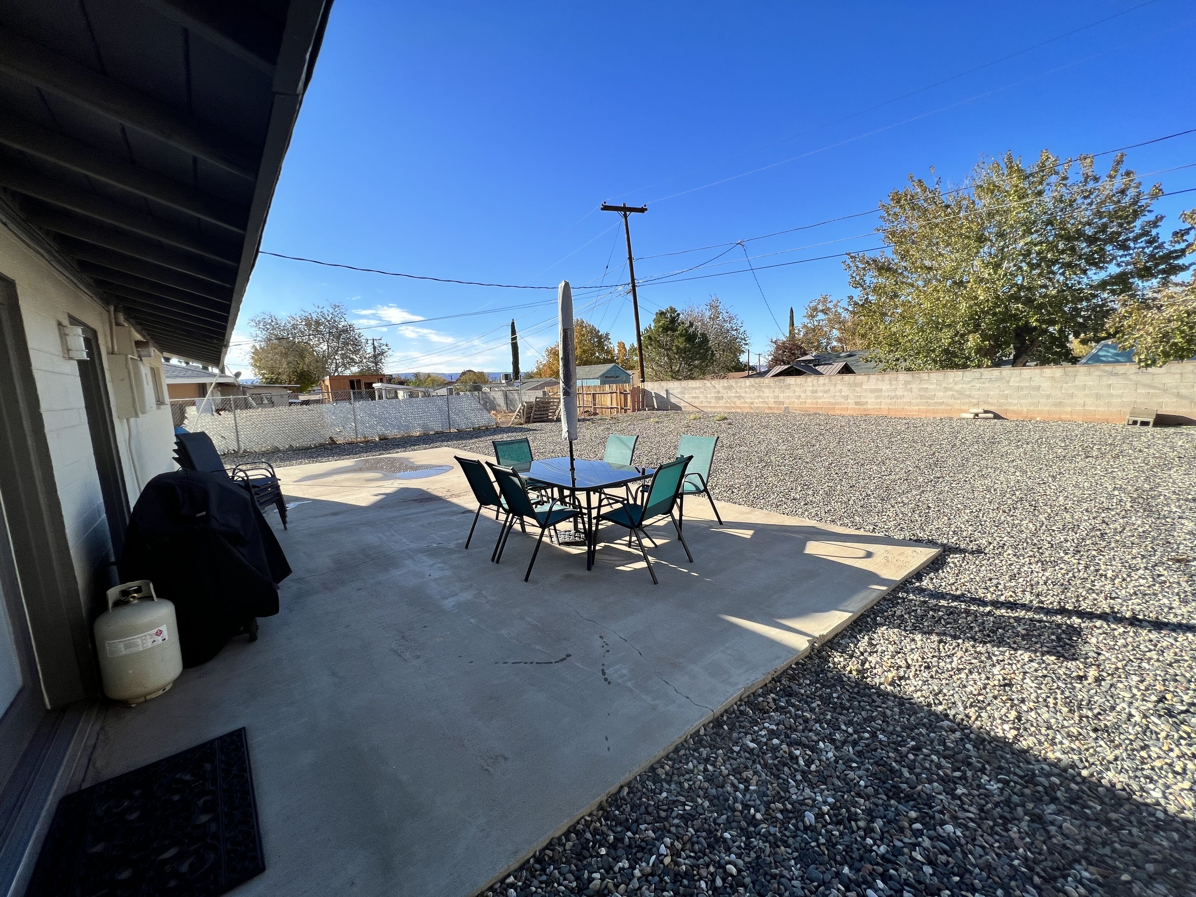 An outdoor patio with a table and chairs, a gas cylinder, and a gravel area.
