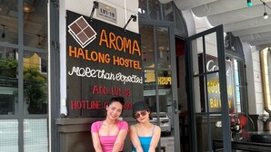 A hostel interior with wooden tables and chairs, a sign reading "Aroma Halong Hostel More than expected", and a visible contact number. - Aroma Ha Long Hostel (Bai Chay)
