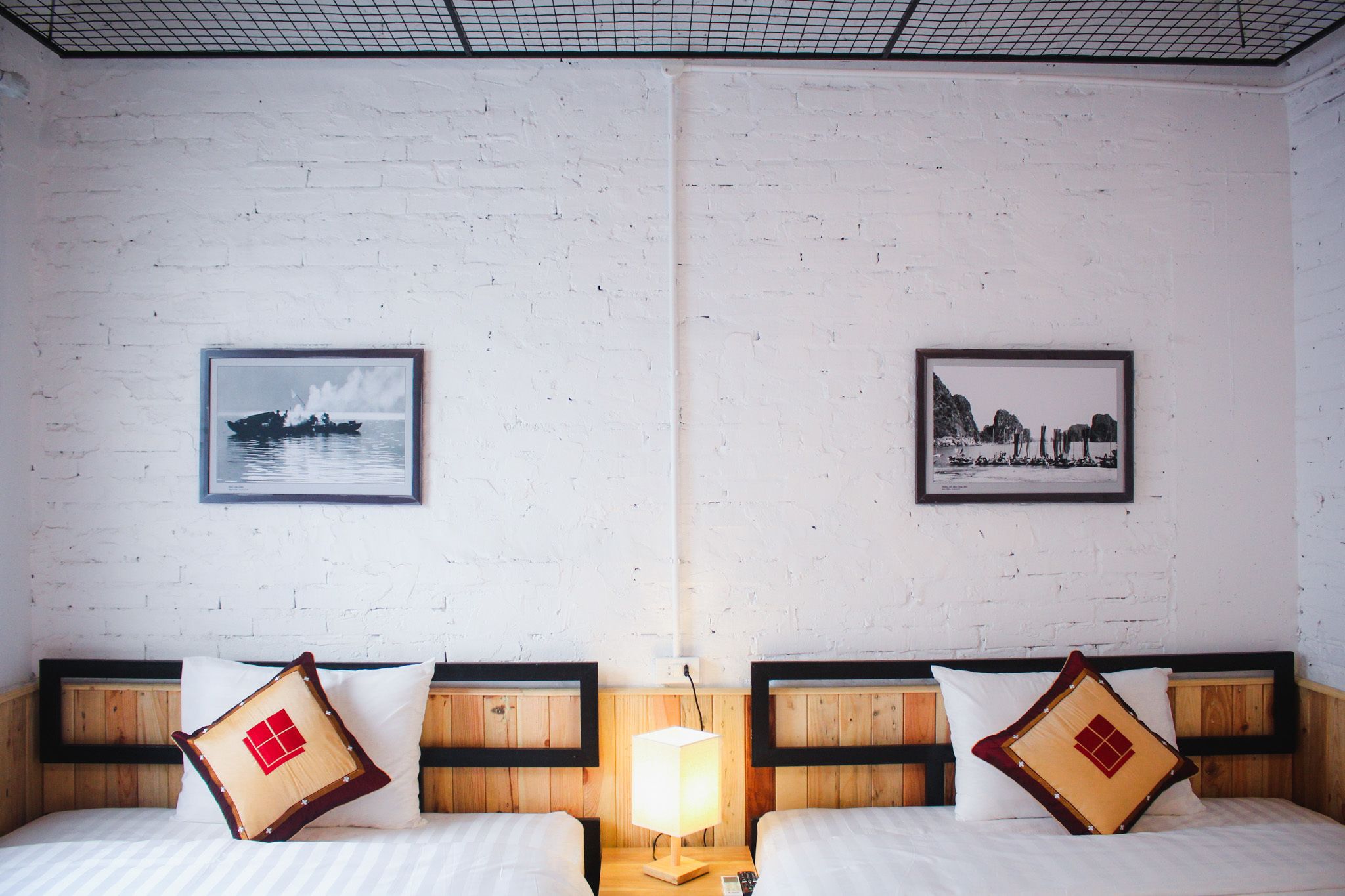A hotel room with two beds, a nightstand with a lamp, and two framed pictures on the wall.