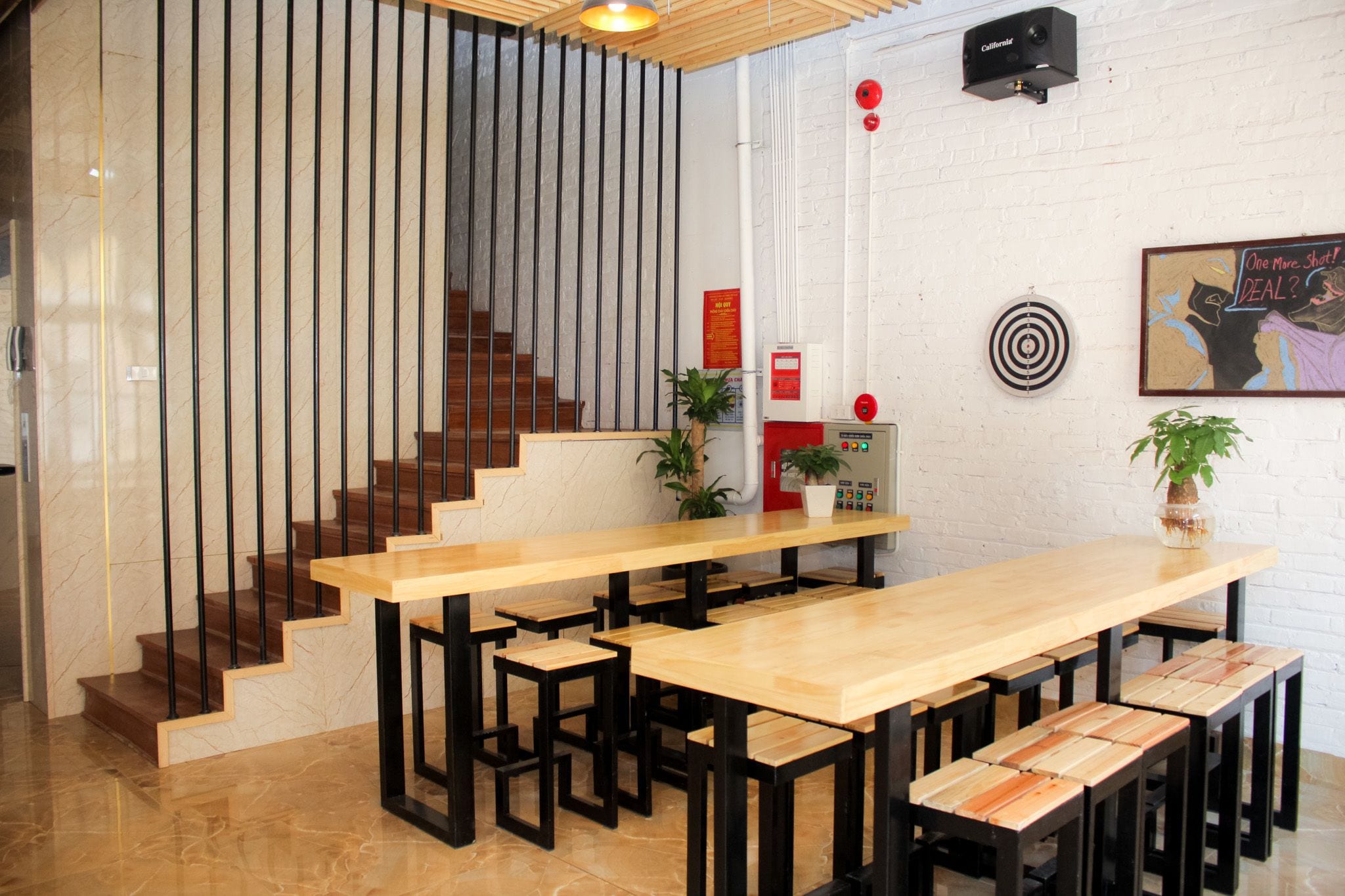 A modern reception area with a wooden reception desk, black metal stools, a staircase with wooden steps, and a white brick wall.