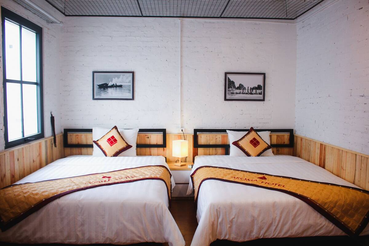 Une chambre d’hôtel avec deux lits, des têtes de lit en bois, une table de chevet avec une lampe et des tableaux encadrés aux murs.