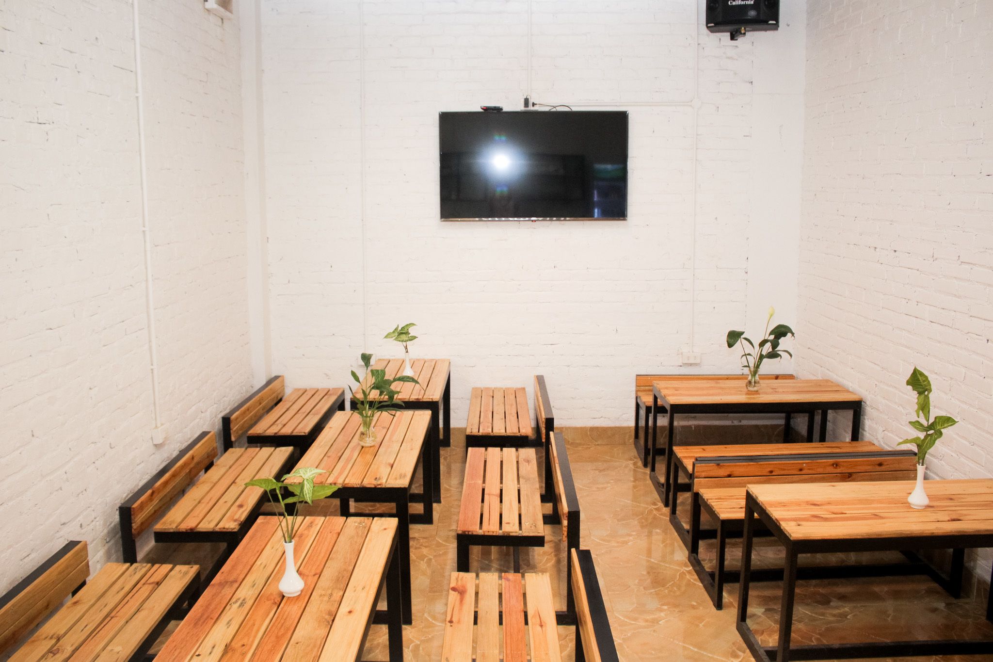A room with wooden tables and benches, a flat-screen TV mounted on the wall, and a white brick wall.