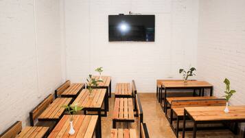 A room with wooden tables and benches, a flat-screen TV mounted on the wall, and a white brick wall.