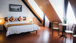 A bedroom with a large bed, two bedside tables with lamps, a small round table with a chair, and a large window with curtains. - Aroma Ha Long Hostel (Bai Chay)