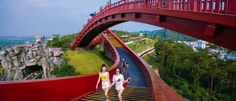 Un puente rojo de diseño curvo, un camino con líneas amarillas y una vista panorámica de la ciudad al fondo.