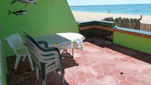 Een terras met een tafel en stoelen, uitzicht op het strand, en twee opgezette vissen aan de muur.