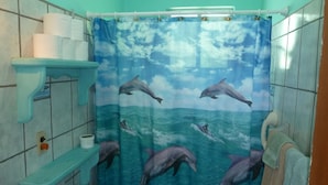 Een badkamer met een douchegordijn waarop dolfijnen in de oceaan zwemmen, een toilet en een plank met toiletpapier.