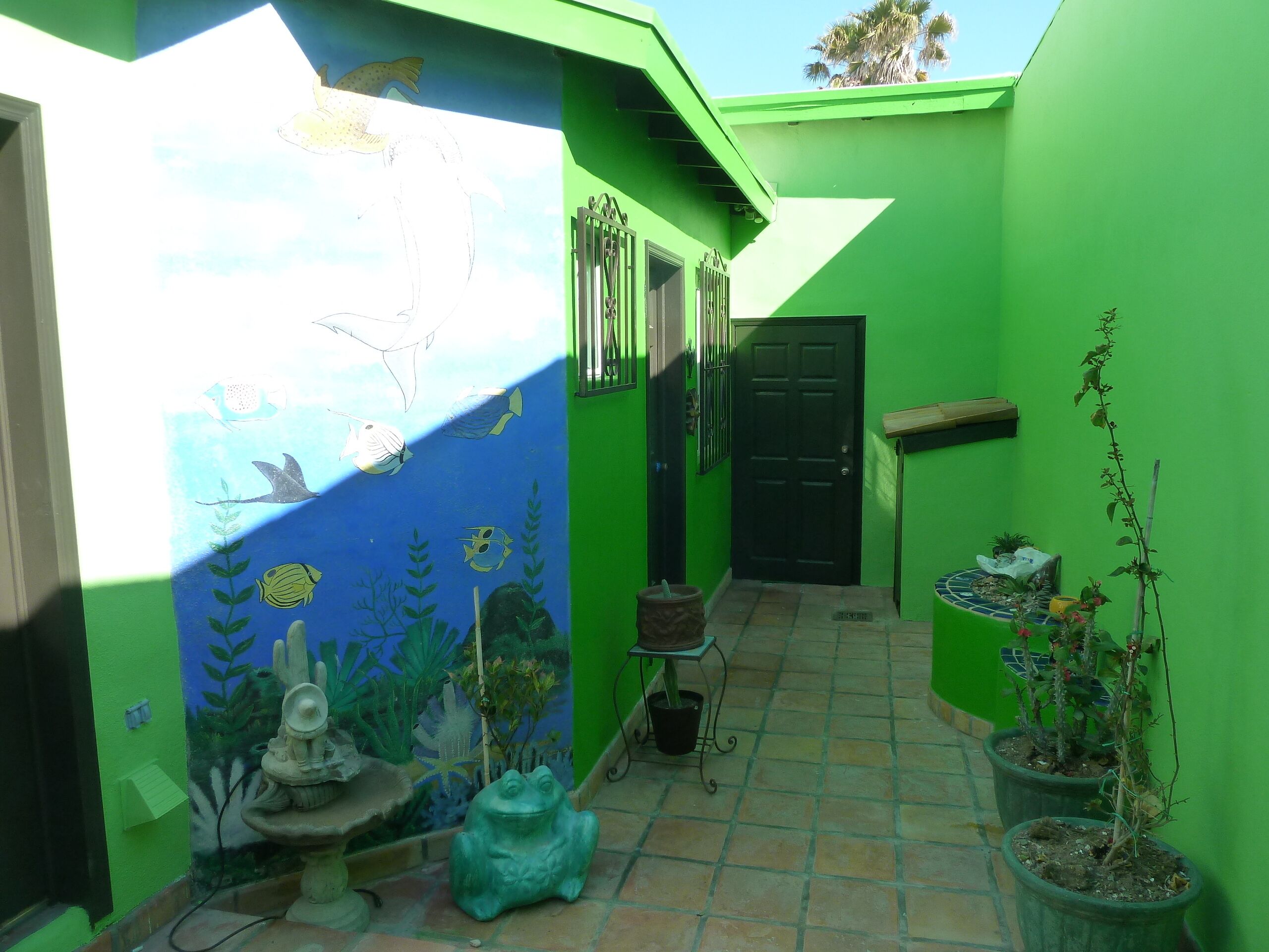 A green-walled interior with a mural of fish and underwater plants, a door, and potted plants.