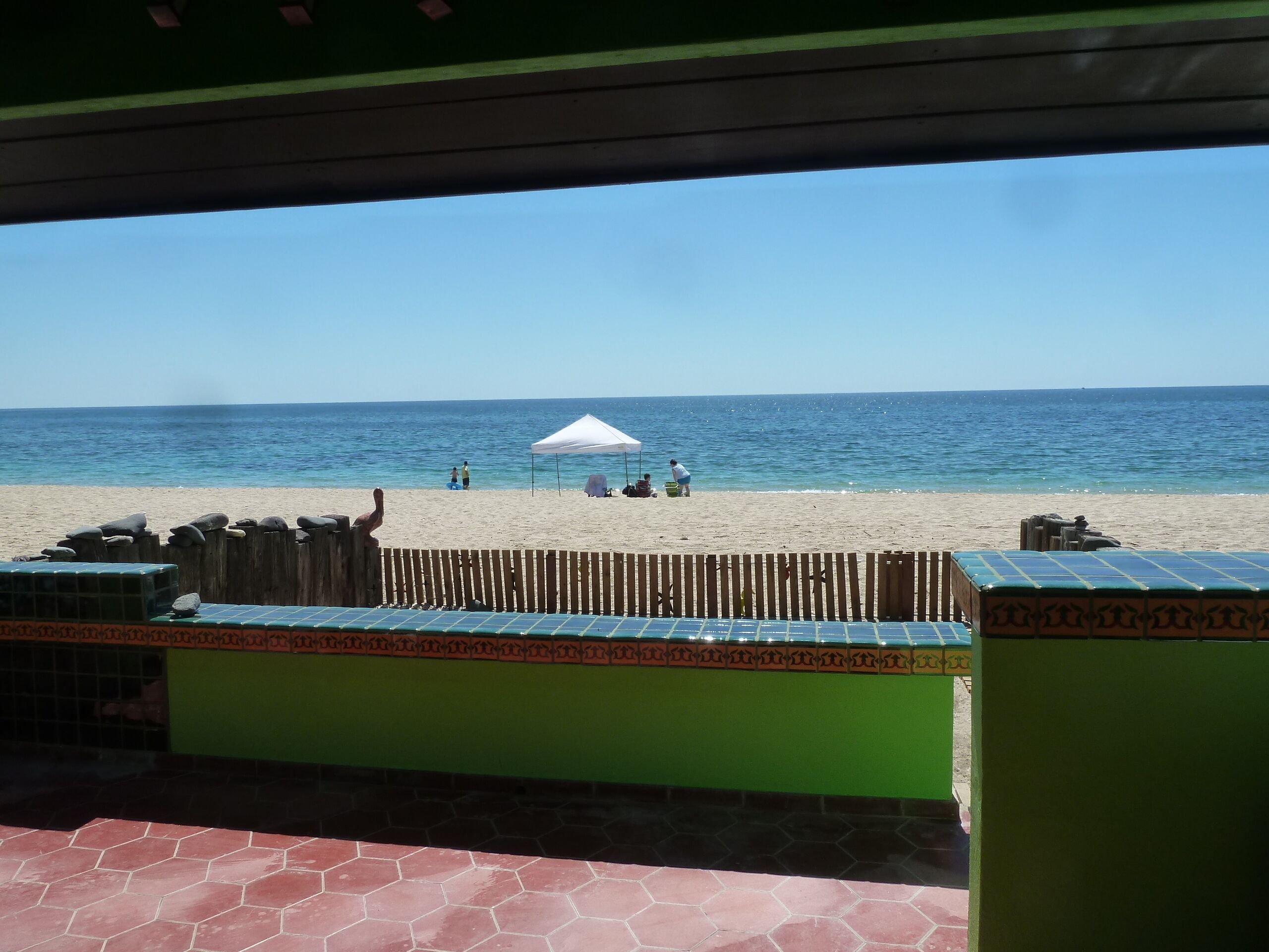 Blick auf einen Strand von einer überdachten Fläche mit Holzzaun und gefliestem Boden.