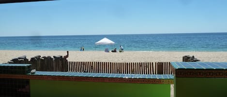 A beach view from a covered area with a wooden fence and tiled floor.