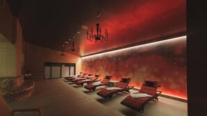 A spa room with multiple red lounge chairs aligned against a wall with a red ambient light. - Hotel Cardinal (Vintu de Jos)