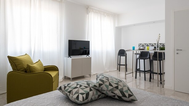 A modern living room with a sofa, a TV, and a dining area with chairs and a table. - Dioniso Comfort Suite by Wonderful Italy (Siracusa)