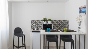 A compact kitchen with a white countertop, two black bar stools, a small refrigerator, and a microwave. There are two potted plants on the counter and a vase with flowers on the right side. - Dioniso Comfort Suite by Wonderful Italy (Siracusa)