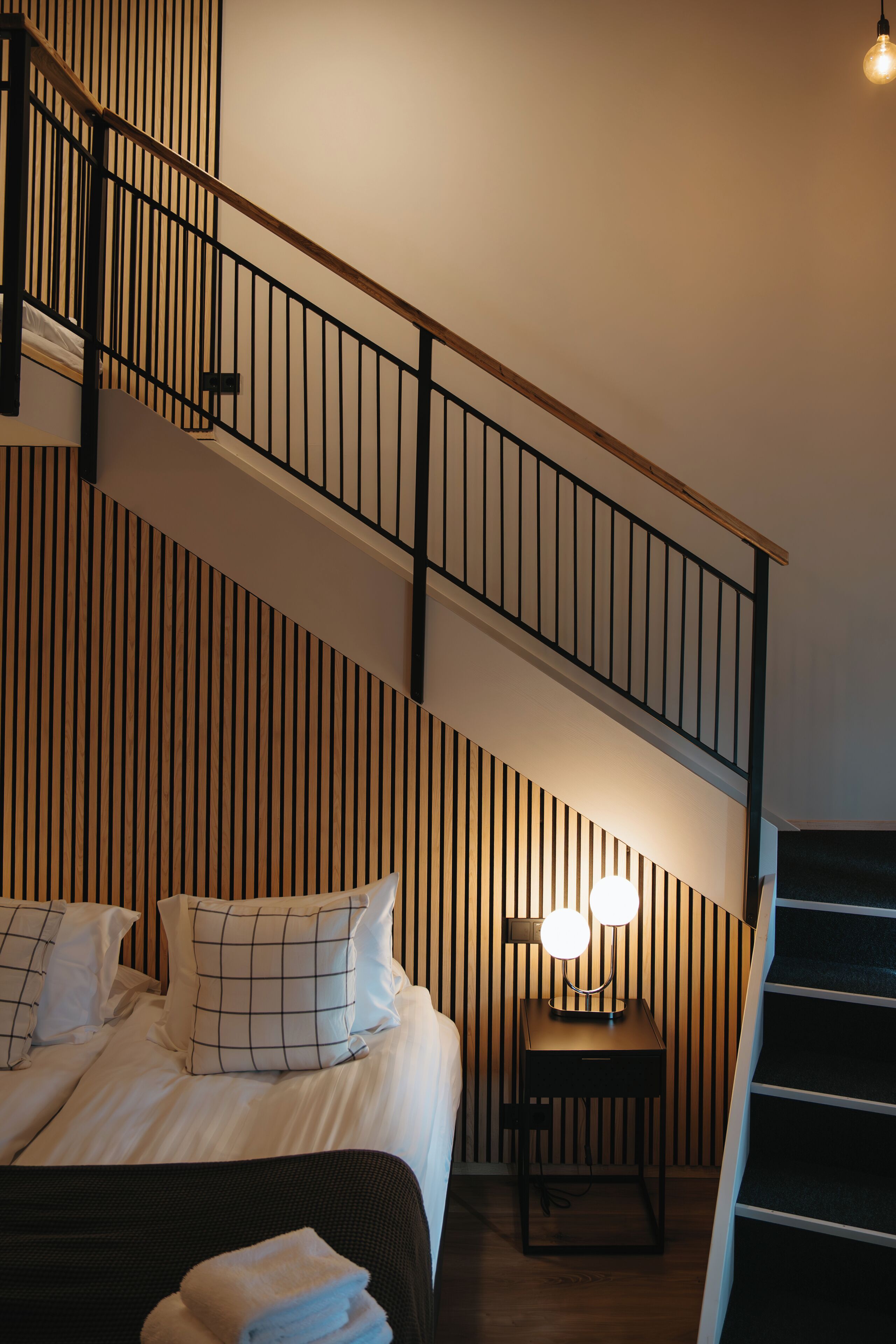 A hotel room with a bed, a nightstand, a lamp, and a staircase.