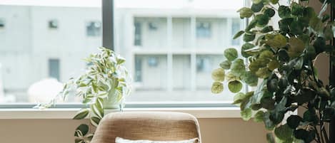 A corner room with a beige armchair, a window with a view of buildings, and a potted plant.