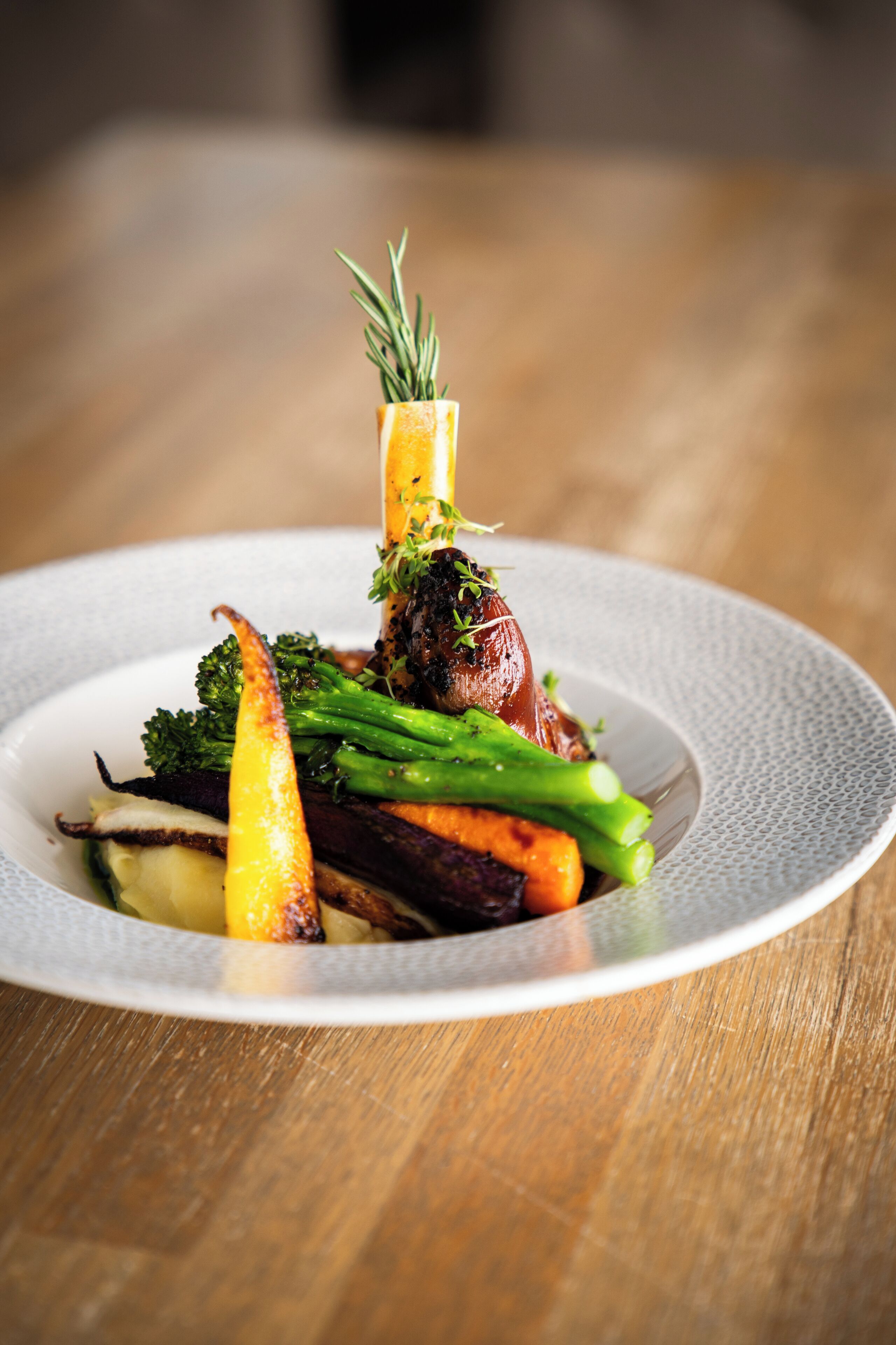 A plate of food with various vegetables and a garnish on a textured plate.