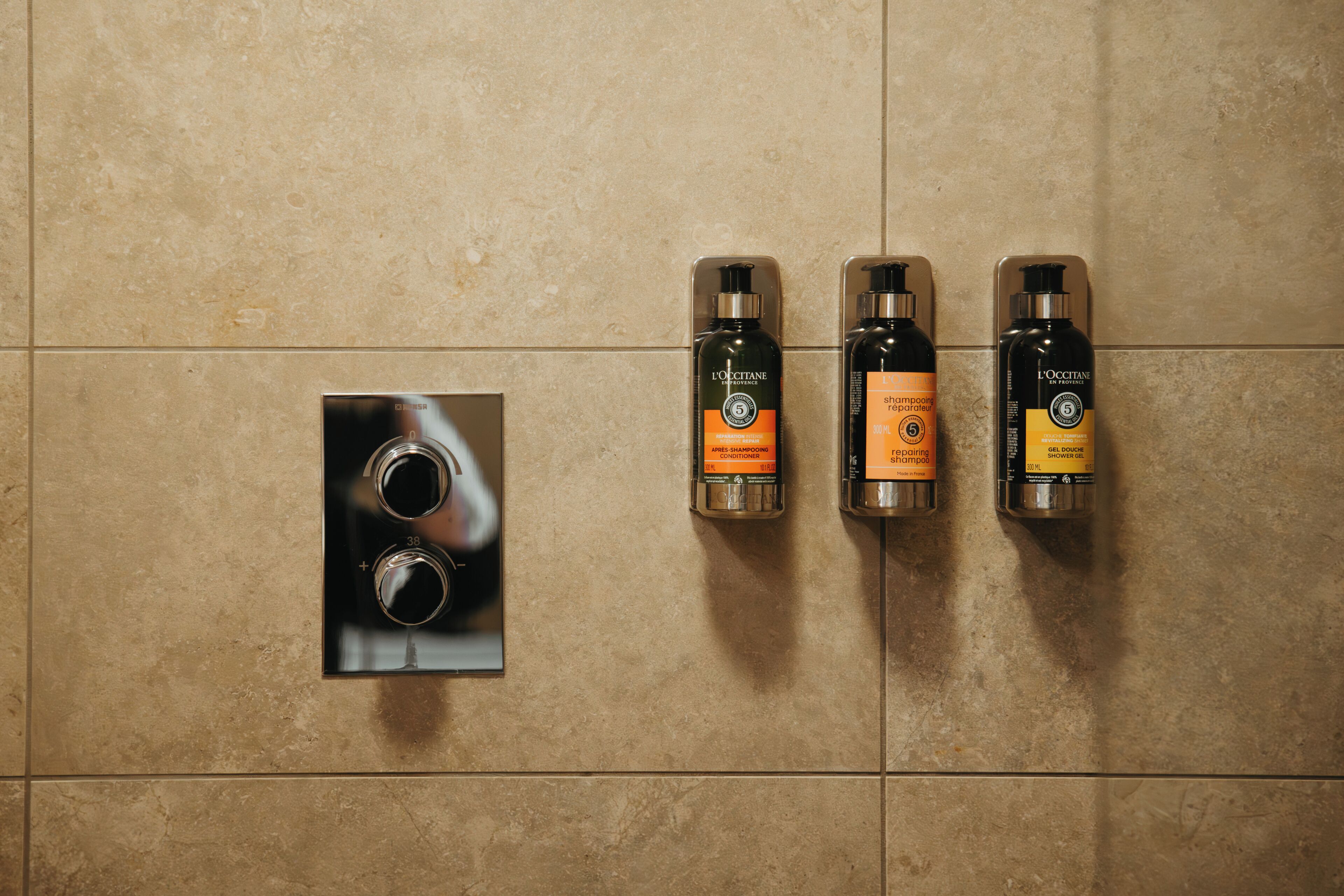 A bathroom with three L'OCCITANE shower bottles and a built-in mirror.