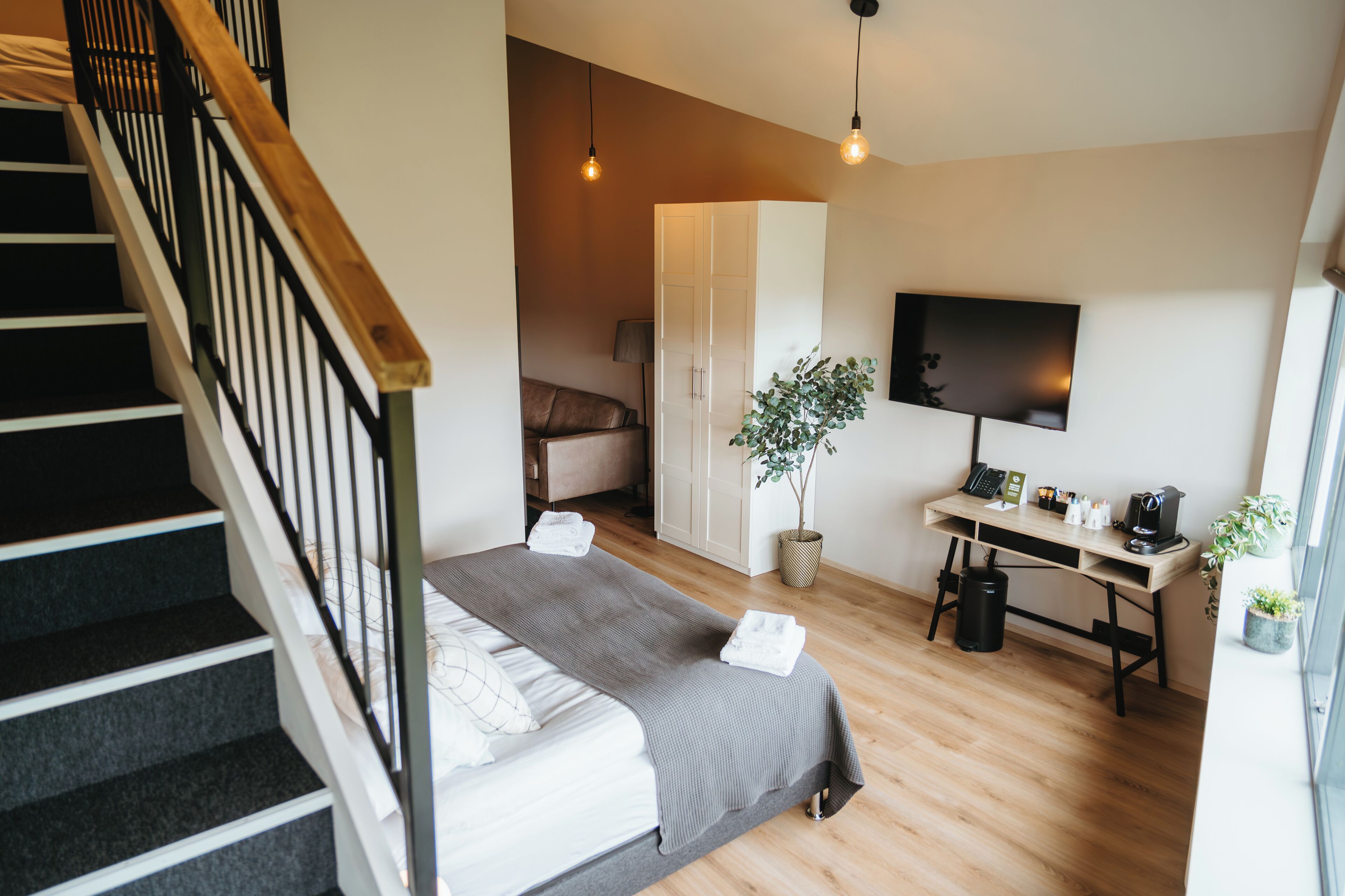 A modern bedroom with a bed, a desk, a TV, and a staircase.