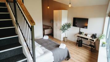A modern bedroom with a bed, a desk, a TV, and a staircase.