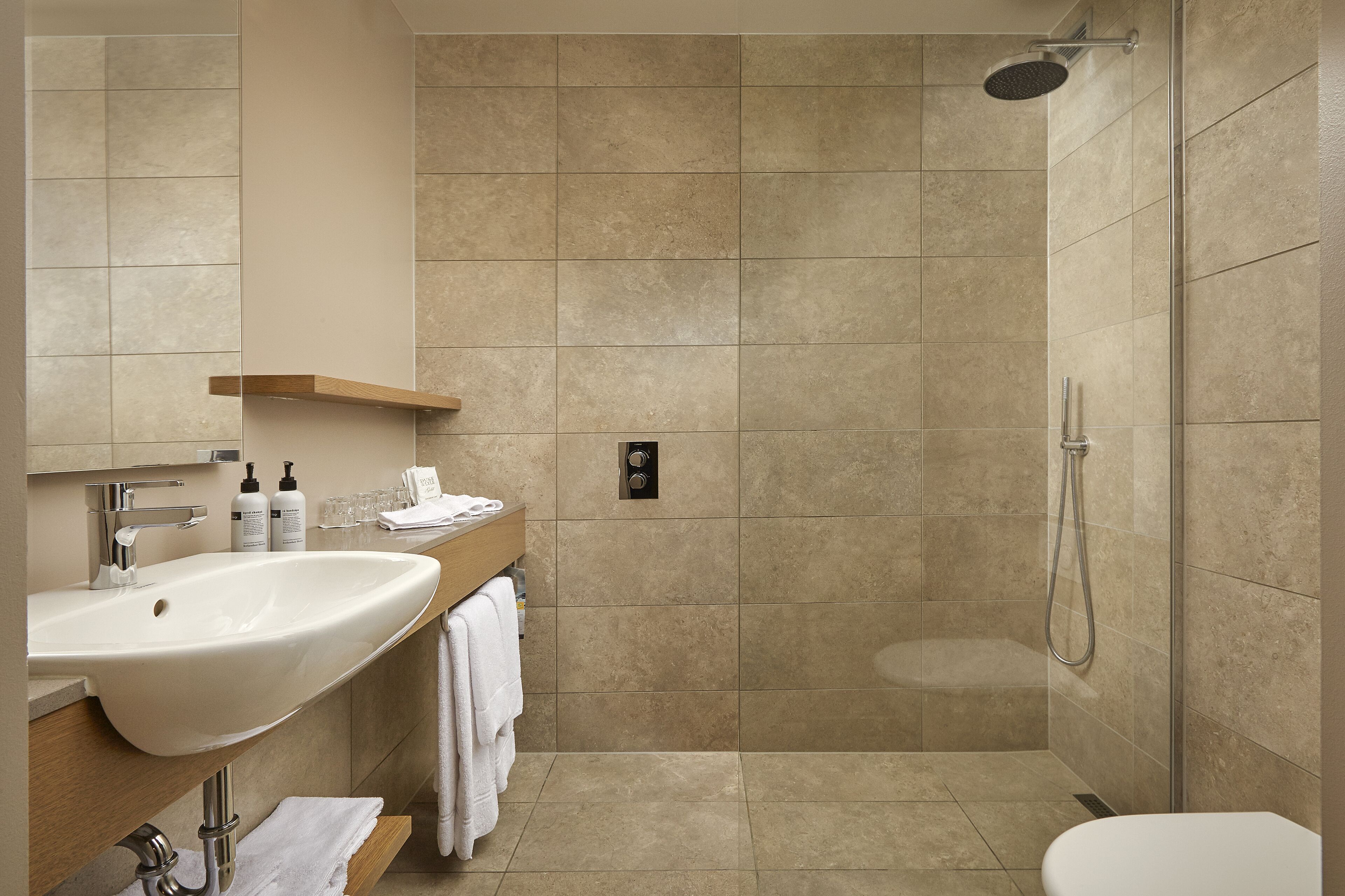 Een moderne badkamer met een groot wastafelmeubel, spiegel en douche.