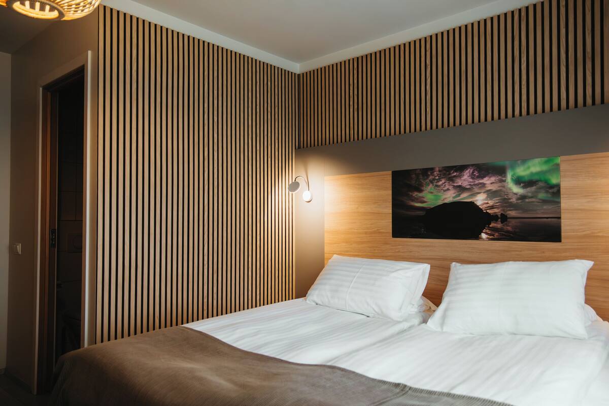 A modern hotel room with a bed, wooden paneling, a wall-mounted picture, and a light fixture.