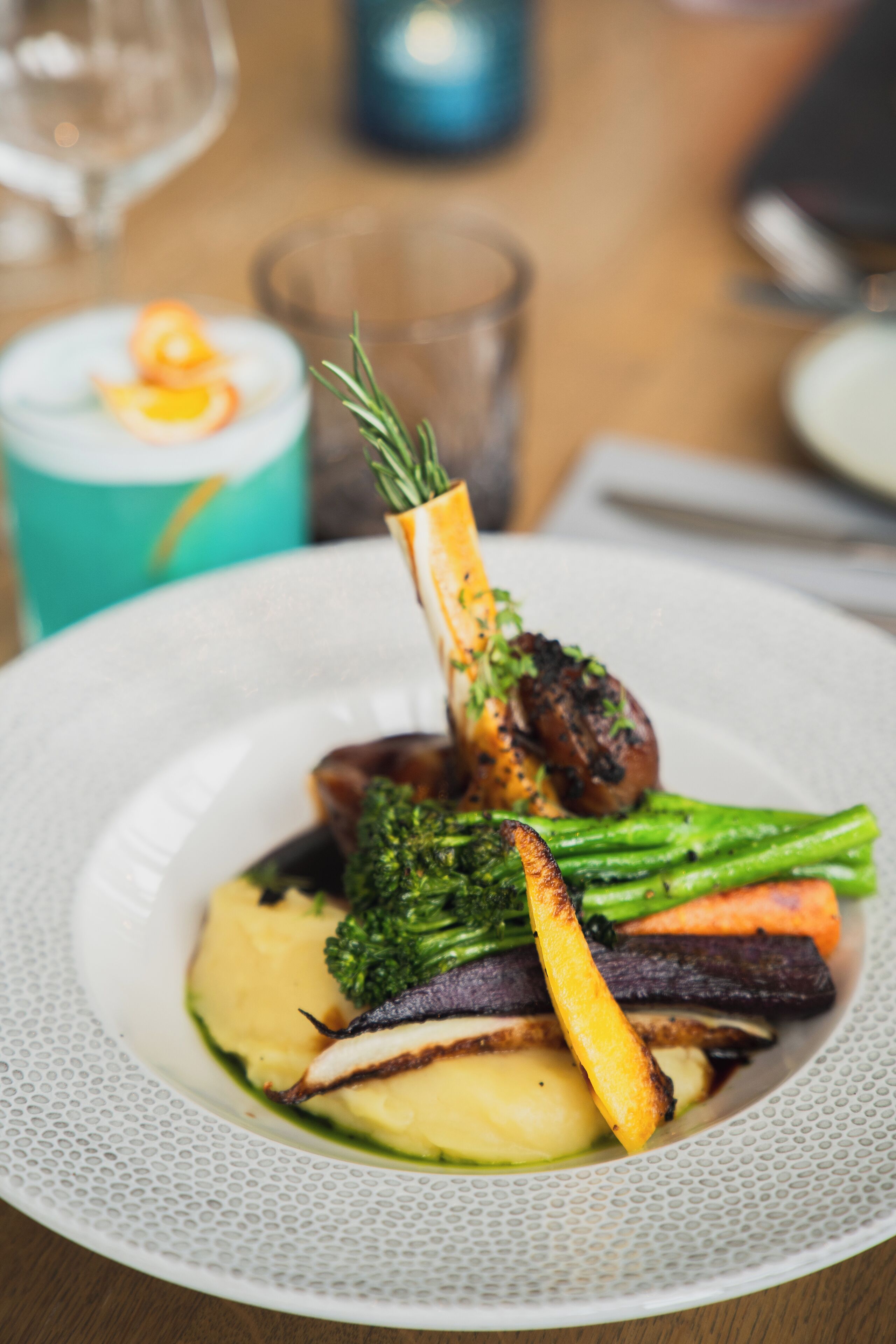 A plate of food with vegetables and a piece of meat, a glass of wine, and a candle in the background.