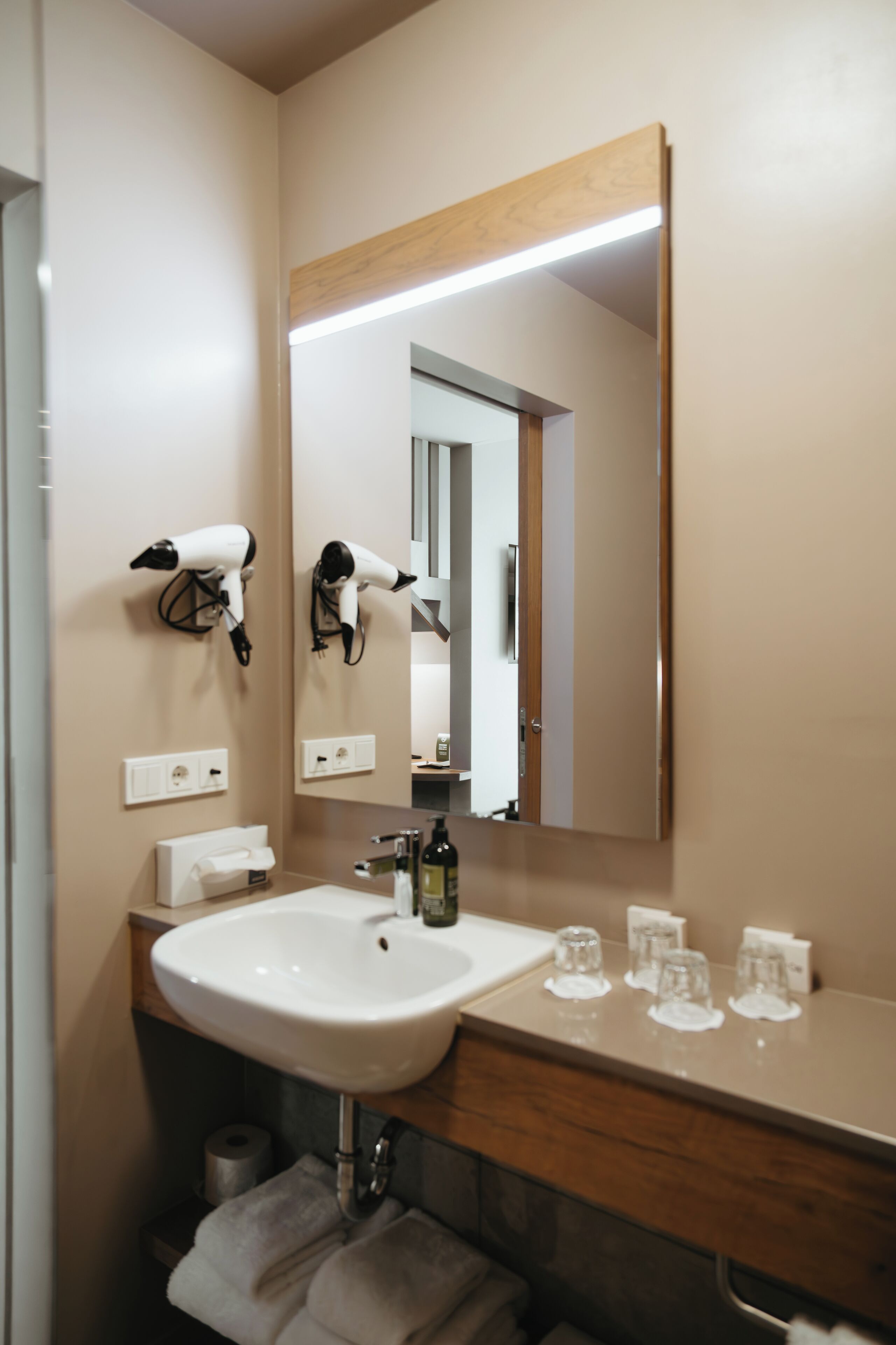 A bathroom with a white sink, a mirror, a hairdryer mounted on the wall, and a towel rack.