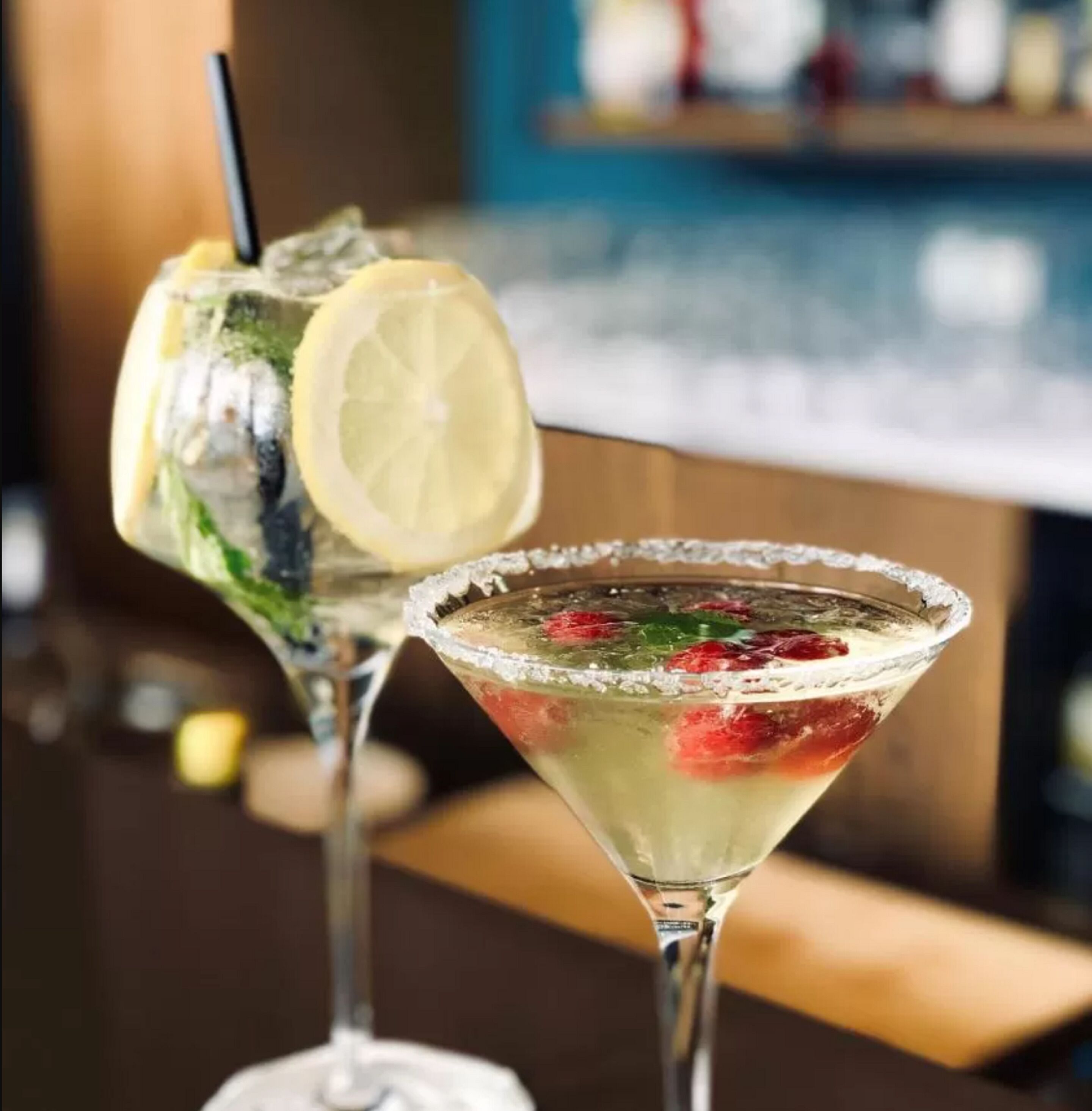 Two cocktails in martini glasses with a salted rim, garnished with lemon slices and mint leaves.