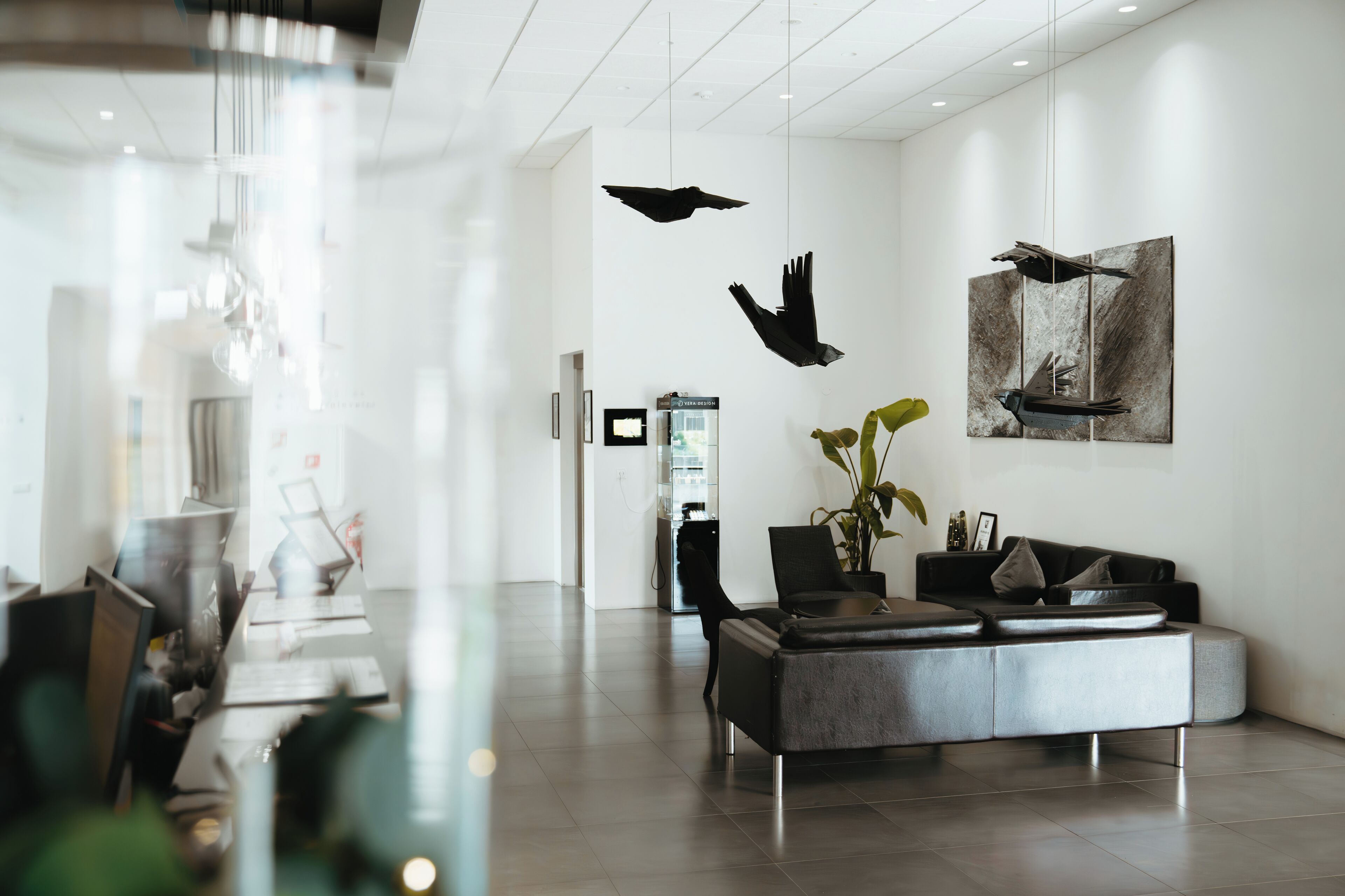 A modern lobby with a minimalist design, featuring a leather sofa, a glass coffee table, and abstract bird sculptures.