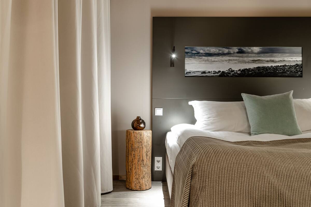 A hotel room with a bed, a nightstand, a wall-mounted picture, and a curtain.