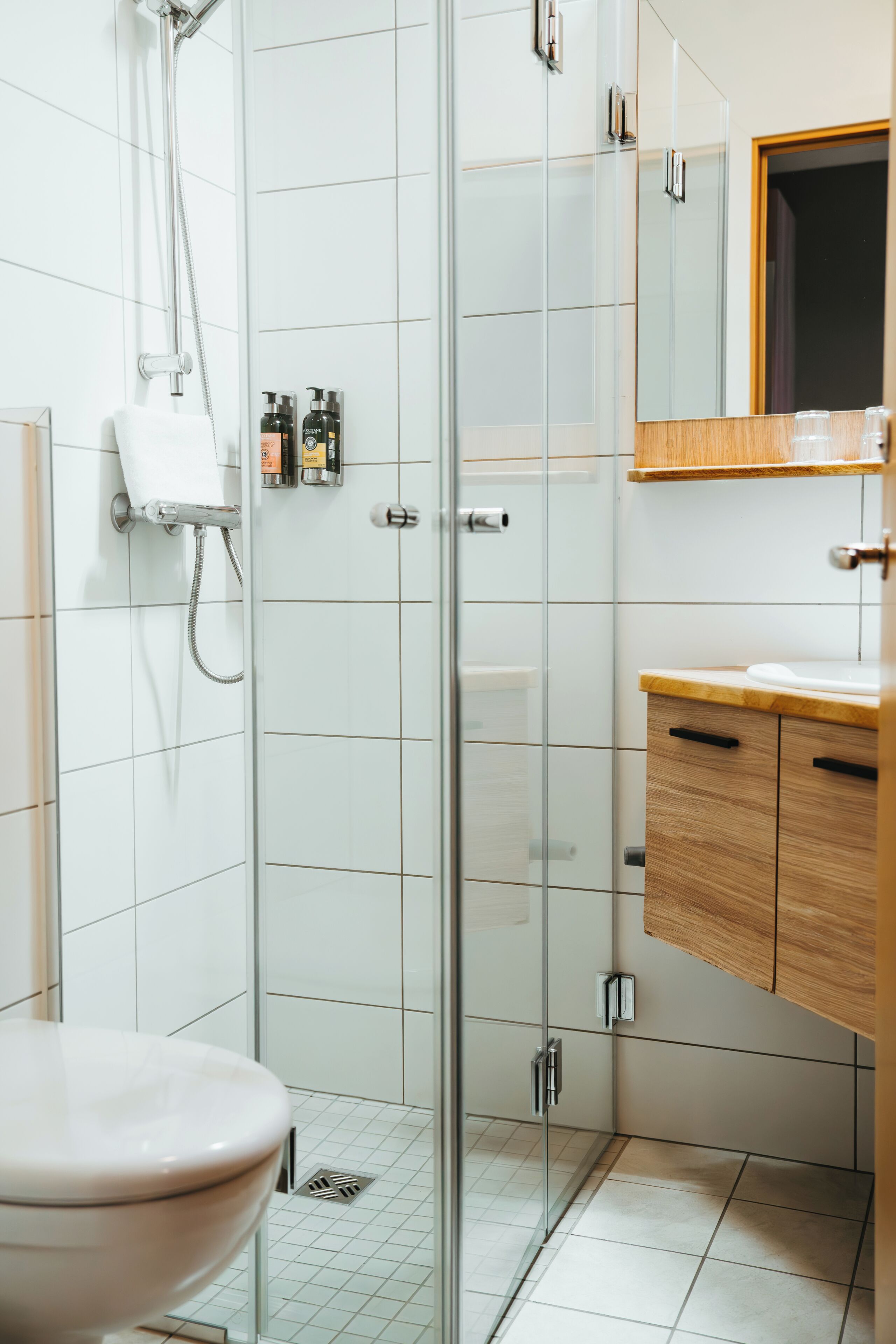 A modern bathroom with a glass-enclosed shower, a white toilet, and wooden cabinets.
