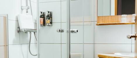 Un baño moderno con ducha envuelta en vidrio, inodoro blanco y muebles de madera.