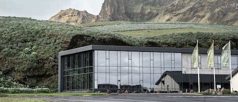 A modern building with large windows and a parking area in front.