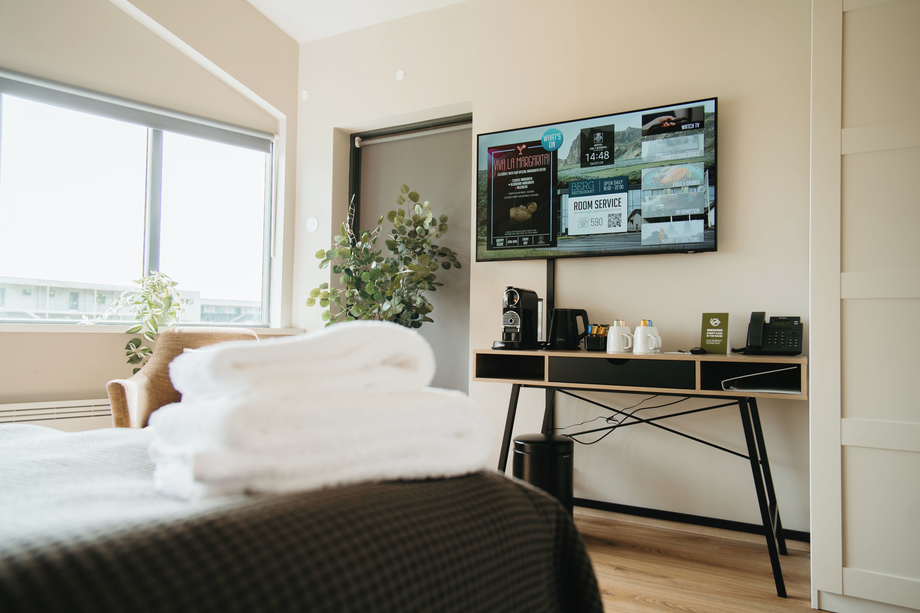 Habitación de hotel con cama, escritorio con computadora, cafetera y televisor mostrando un menú.