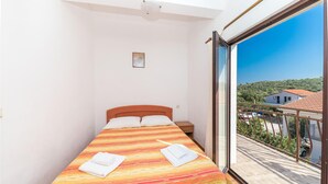 A small bedroom with a bed, a nightstand, and a window with a view of a hillside and buildings. - 1 bedroom awesome apartment in Okrug Donji (Okrug Donji)