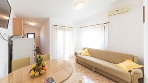 A compact living space with a kitchenette, a dining area with a fruit bowl, a sofa with a yellow pillow, and a TV mounted on the wall. - 1 bedroom awesome apartment in Okrug Donji (Okrug Donji)