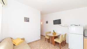 A compact living space with a sofa, a dining table with chairs, a TV mounted on the wall, and a refrigerator. - 1 bedroom awesome apartment in Okrug Donji (Okrug Donji)