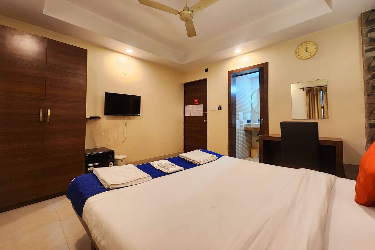 Quarto de hotel com cama, ventoinha no teto, televisão, espelho e porta do banheiro.