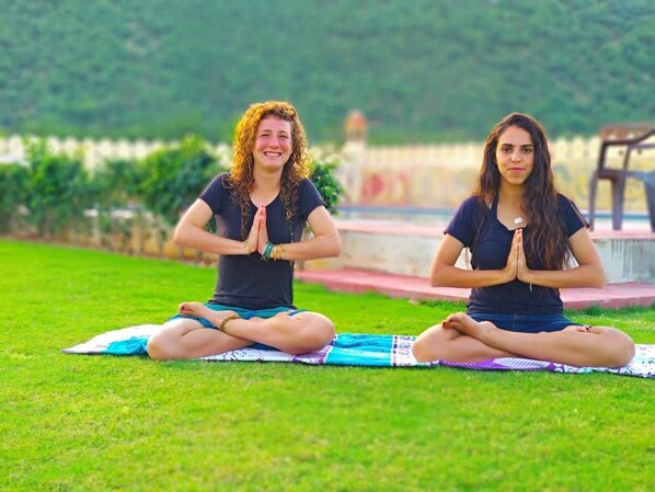 Two individuals seated on yoga mats in a grassy outdoor area. - Parvat Valley Resort (Pushkar)