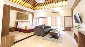 A modern hotel room with a wooden ceiling, a large bed, a sofa, a TV, and a desk. - Luminor Hotel Banyuwangi Yos Sudarso by WH (Banyuwangi)