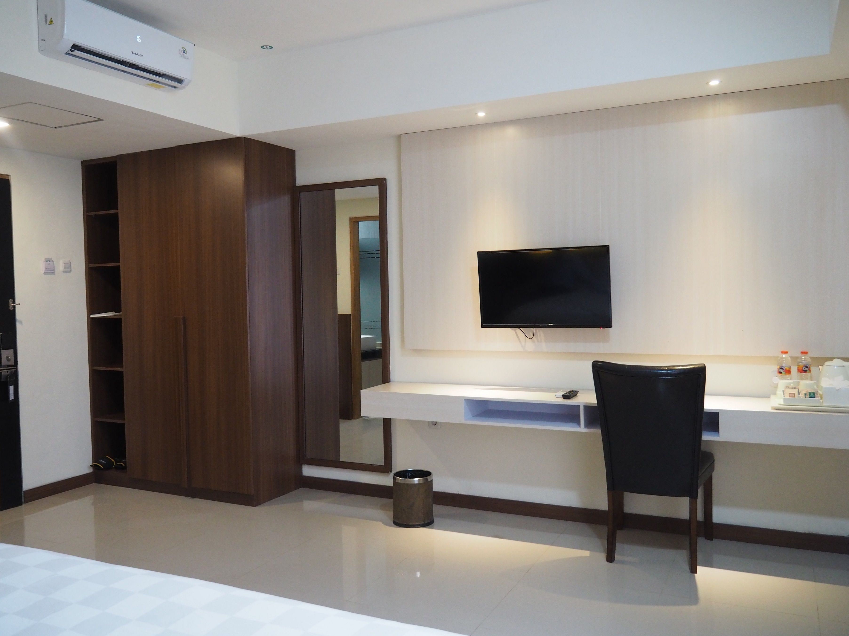 Ein modernes Schlafzimmer mit großem Kleiderschrank, Schreibtisch mit Stuhl, Wand-Fernseher und Mülleimer.