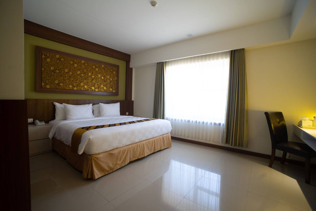 Une chambre d’hôtel avec un grand lit, un bureau avec une chaise, un téléphone et une fenêtre avec des rideaux.