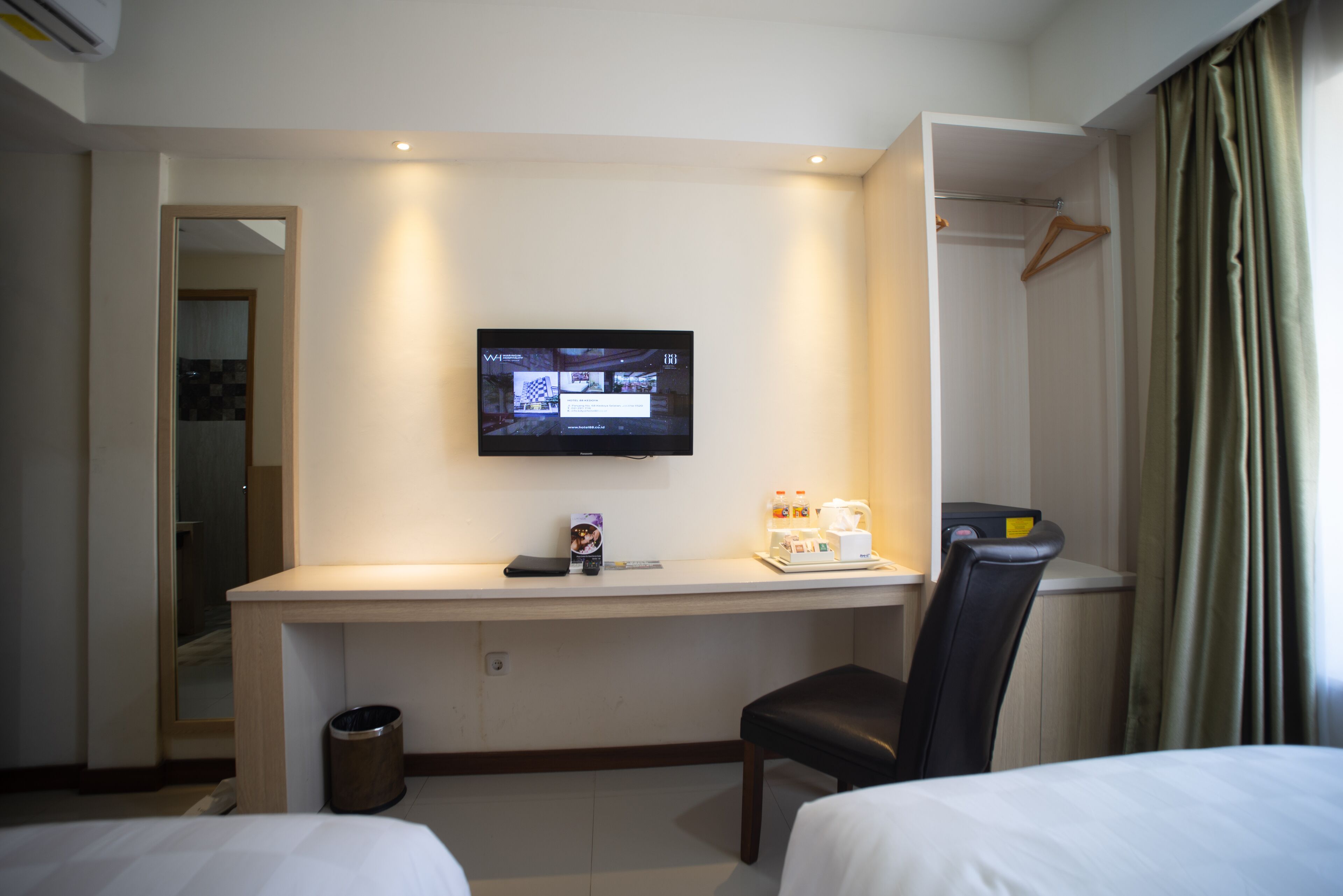 Een hotelkamer met een bed, een bureau met een televisie, een stoel en een kapstok.