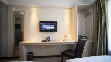 Een hotelkamer met een bed, een bureau met een televisie, een stoel en een kapstok.