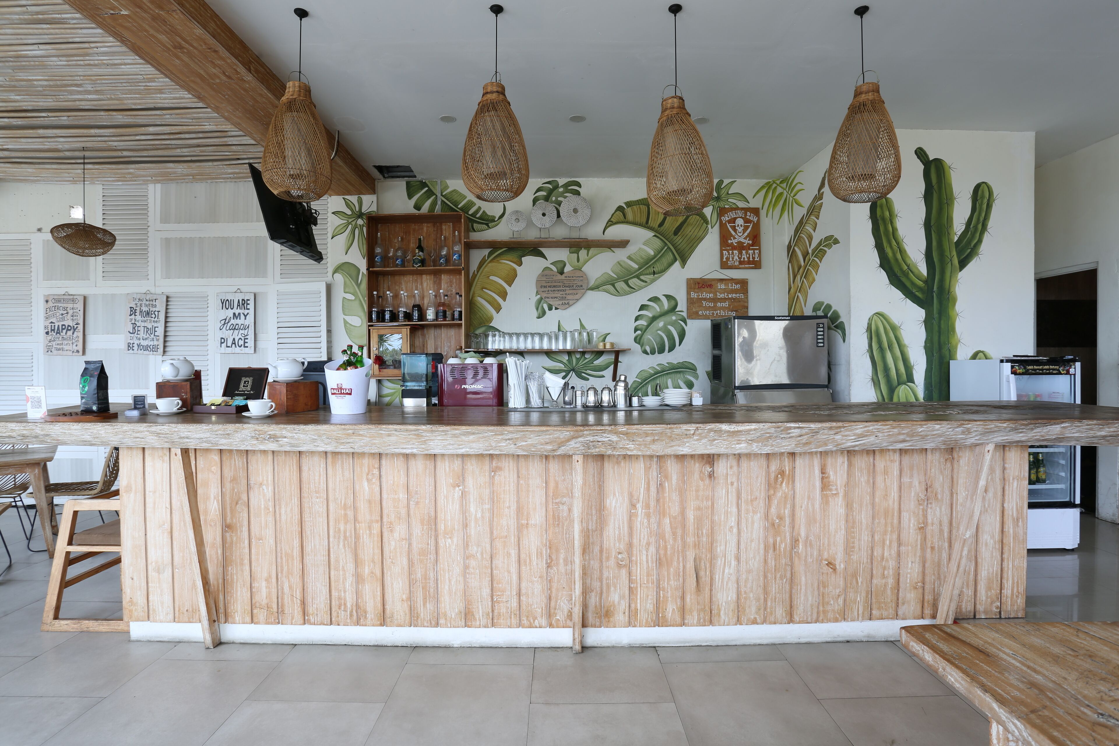 A kitchen with a wooden island, hanging wicker lights, and a wall mural of plants and cacti.