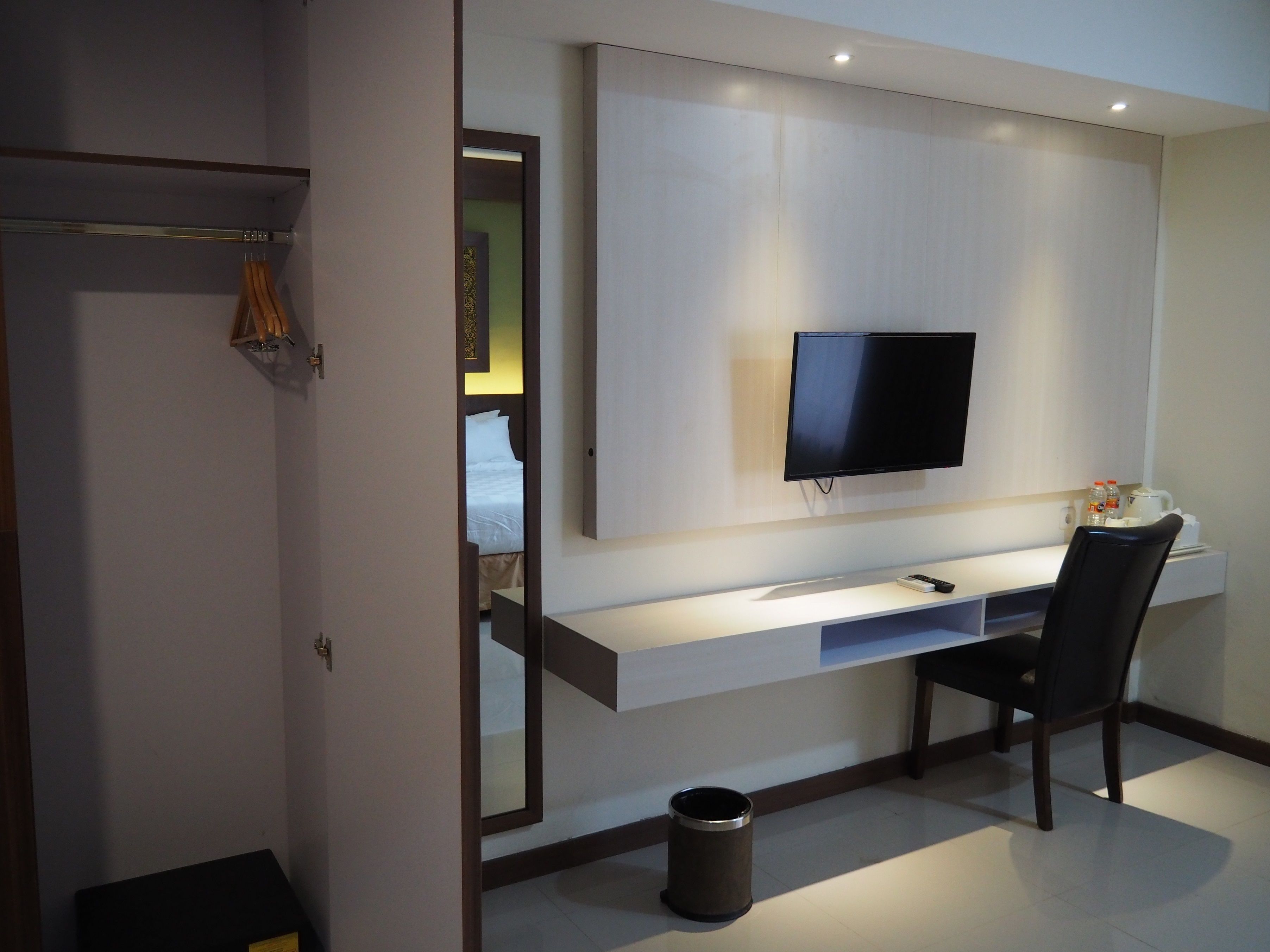 Una habitación de hotel moderna con televisión de pantalla plana en la pared, un escritorio con silla y un cubo de basura pequeño.